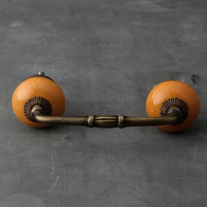 May include: A pair of orange ceramic drawer pulls with a brass finish and a simple, curved design.