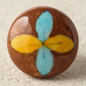 Może przedstawiać: Okrągły ceramiczny gałka z brązowym tłem i wzorem niebieskiego i żółtego kwiatu.