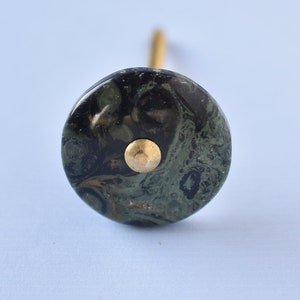 May include: A round, green and black marble knob with a gold metal accent. The knob is attached to a gold metal screw.
