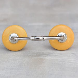 May include: A pair of yellow ceramic drawer pulls with a silver metal connecting bar.