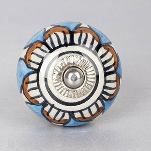 Puede incluir: Un pomo de cerámica azul y blanco con un diseño floral marrón y negro. El pomo tiene una base de metal plateado.