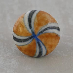 May include: A round, ceramic bead with a warm orange base color. The bead features a spiral design of alternating white, black, and blue stripes. The stripes converge at the center, creating a visually appealing pattern. The bead has a glossy finish.
