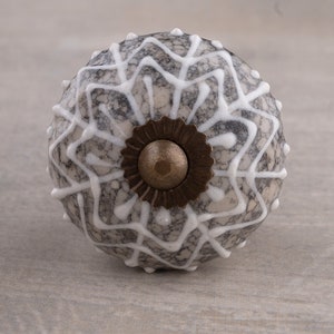 Puede incluir: Un pomo de cerámica gris y blanco con un patrón geométrico blanco y una base de metal marrón.