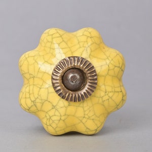 May include: A yellow ceramic knob with a crackled glaze and a brass-colored metal base. The knob has a flower-like shape with six rounded petals.