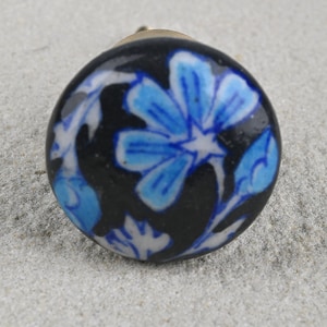 Pode incluir: Um botão de cerâmica preto com um design floral azul e branco. O botão tem um caule de metal dourado.