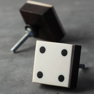 May include: Two black and white square cabinet knobs with a silver screw. The knobs have a white surface with four black dots.
