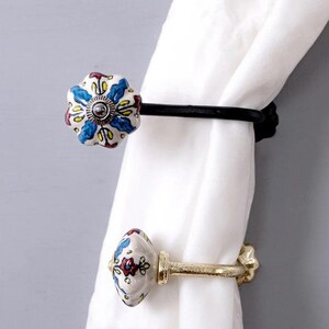 May include: Two decorative curtain tiebacks with floral patterned ceramic knobs. One tieback is black metal and the other is gold metal.