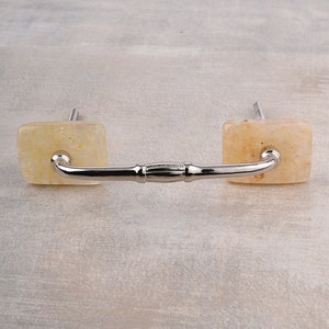 May include: A silver cabinet pull with square, light yellow, marbled ends.