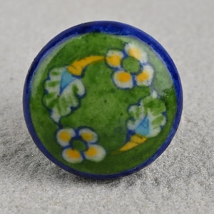 May include: A green ceramic knob with a blue rim and a floral design in yellow, white, and blue.