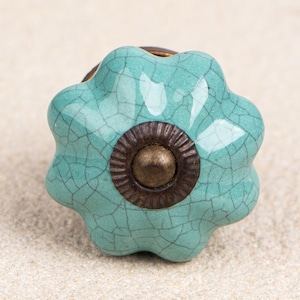 Puede incluir: Un pomo de armario de cerámica azul turquesa con un esmalte craquelado y un centro de color bronce con borde dorado.