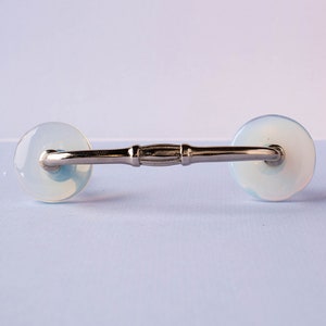 May include: A silver cabinet pull with two round, translucent white knobs. The knobs have a slight blue tint.