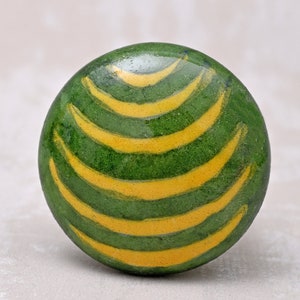 May include: A round, green decorative object with yellow, curved stripes. The object has a smooth, glossy finish and a watermelon-like pattern. The design is simple and eye-catching, suitable for home decor.