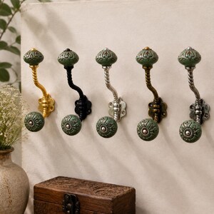 Puede incluir: Cinco ganchos de pared con pomos de cerámica verde salvia y patrones en relieve. Cada gancho tiene un brazo de metal trenzado en varios acabados, incluyendo oro, negro, plata, bronce y plata envejecida, con un pomo de cerámica a juego.