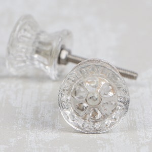 May include: Two clear glass cabinet knobs with a floral design. The knobs have a silver metal screw.
