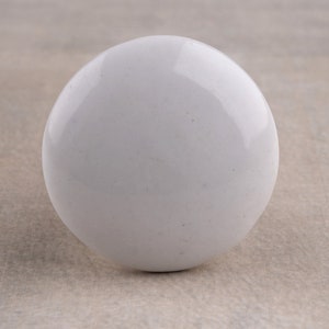 Puede incluir: Un pomo esférico blanco y liso con un acabado brillante y reflectante. El objeto tiene un color blanco sólido y uniforme en toda su superficie redondeada, presentando una forma circular limpia y sencilla desde esta perspectiva frontal.