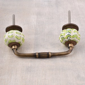 Puede incluir: Un pomo de armario de cerámica verde y blanco con una manija de latón. El pomo tiene un patrón geométrico.