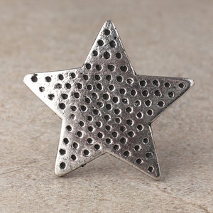 Puede incluir: Un adorno plateado en forma de estrella con una superficie texturizada. La estrella está hecha de metal y tiene un patrón de puntos.