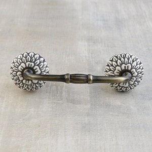 May include: A white ceramic drawer pull with a floral design and a brass finish. The pull has a simple, elegant design and would be a great addition to any kitchen or bathroom.