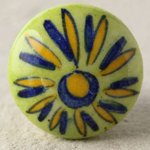 Può includere: Un pomello in ceramica verde con un motivo floreale giallo e blu. Il pomello è rotondo e ha una superficie liscia.