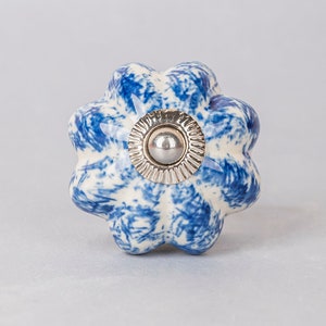 Può includere: Pomo in ceramica blu e bianco con un centro argentato. Il pomo ha una forma a fiore con sei petali.