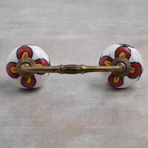 May include: A pair of white ceramic drawer pulls with a floral design in red, yellow, and green. The pulls are connected by a brass bar.