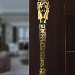 May include: A gold lion head door handle with a textured body. The handle is mounted on a dark brown wooden door.