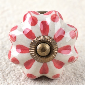 May include: A white ceramic knob with a pink floral pattern and a brass centre. The knob has a five-pointed star shape.