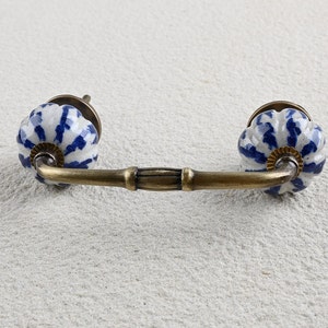May include: A white ceramic cabinet knob with a blue and white floral pattern. The knob is attached to a brass bar handle.