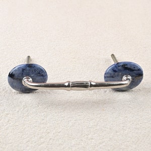 May include: A silver cabinet pull with a blue and white marble design on each end. The pull has a curved shape and a decorative center.