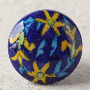 Könnte beinhalten: Ein blauer Keramik-Knopf mit einem Blumenmuster. Der Knopf zeigt gelbe Blumen mit grünen Zentren und blauen Blättern auf einem dunkelblauen Hintergrund.