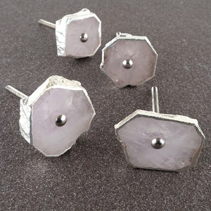 Może przedstawiać: Cztery różowe kryształowe gałki do szafek z srebrnymi metalowymi akcentami. Każda gałka ma okrągły srebrny metalowy element w środku.