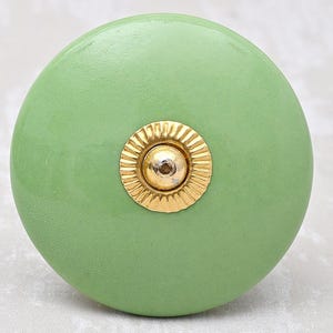 Op de afbeelding: Een ronde, groene keramische kastknop met een gouden metalen accent. De knop heeft een gladde, matte afwerking.