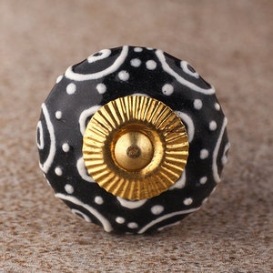 May include: Black ceramic knob with a white swirl and dot pattern. The knob has a gold metal center.