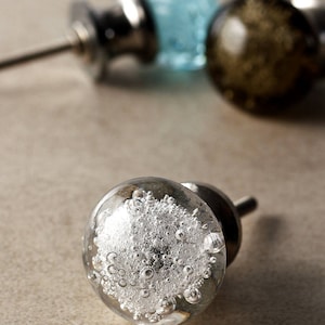 Peut inclure: Un bouton de porte en verre transparent avec une base en métal argenté. Le verre est rempli de petites bulles d'air.