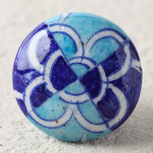 May include: A blue and white ceramic knob with a geometric pattern. The knob has a circular shape and is decorated with a repeating design of interlocking circles and swirls.