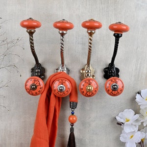 May include: Four orange ceramic hooks with a clock face design. The hooks are mounted on a wall and have a twisted metal stem. One hook has a scarf hanging from it.