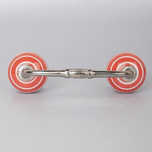 May include: A silver drawer pull with two round ceramic knobs. The knobs are orange with white stripes.