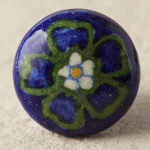 May include: A blue ceramic knob with a green and white floral design. The flower has a white center with a yellow dot.