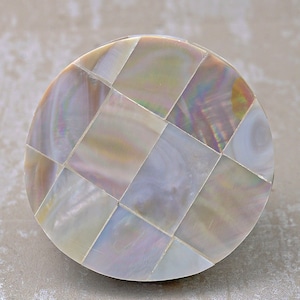 Pode incluir: Um botão redondo de madrepérola branca iridescente com um padrão xadrez.