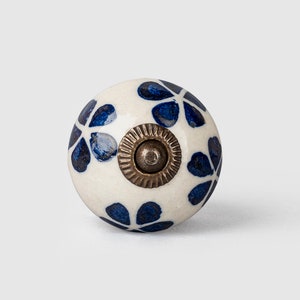 Puede incluir: Pomo de cerámica blanco con un patrón floral azul y un tornillo de latón.