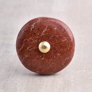 May include: A round, red, marbled knob with a gold metal accent. The knob is perfect for adding a touch of rustic charm to any cabinet or drawer.