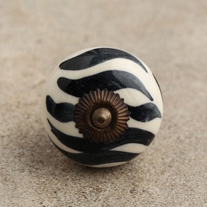 May include: Black and white zebra patterned ceramic knob with a gold metal accent.