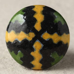 Könnte beinhalten: Ein runder Keramik-Knopf mit einem geometrischen Muster in Schwarz, Gelb und Grün.