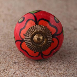 Può includere: Pomello per armadio rotondo in ceramica rossa con un motivo floreale arancione e nero. Il pomello ha una base in metallo color ottone. Accenti verdi a forma di foglia sono sparsi sulla superficie. Questo hardware decorativo aggiunge un tocco di colore.