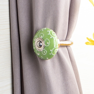 Puede incluir: Atado de cortina de cerámica verde con un patrón de remolino blanco. El atado tiene un anillo de metal plateado.