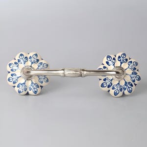 May include: A white ceramic drawer pull with a blue floral design and a silver metal bar connecting the two knobs.