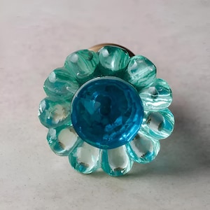 May include: A teal blue and light blue glass flower-shaped knob with a round center. The knob is perfect for adding a touch of whimsy to any cabinet or drawer.