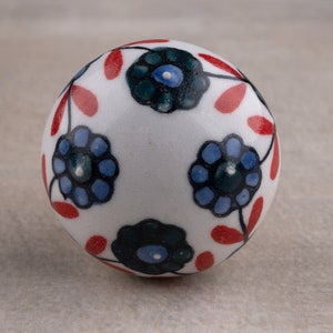 May include: A white ceramic cabinet knob with a floral design. The knob features blue and dark green flowers with red leaf accents. The round knob is a decorative element for furniture.