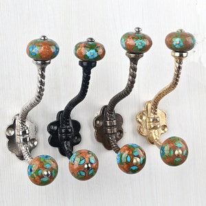 May include: Four wall hooks with twisted metal stems and floral ceramic knobs. The hooks feature different metal finishes including silver, black, bronze, and gold. Each knob has a brown base with blue and green painted flower patterns.