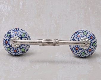 May include: A pair of ceramic drawer pulls with a blue and white floral pattern. The pulls are attached to a silver metal bar.